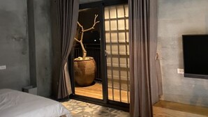 A bedroom with a bed, a bench, a TV, and a view through a glass door. - Green House Homestay (Magong)