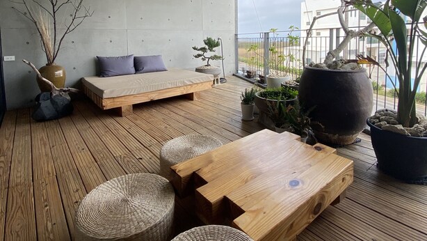 A modern outdoor seating area with wooden flooring, a sofa, and a dining table. - Green House Homestay (Magong)