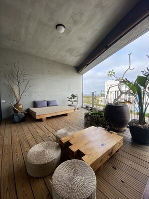 Un área de estar moderna al aire libre con suelo de madera, un sofá y una mesa de comedor.