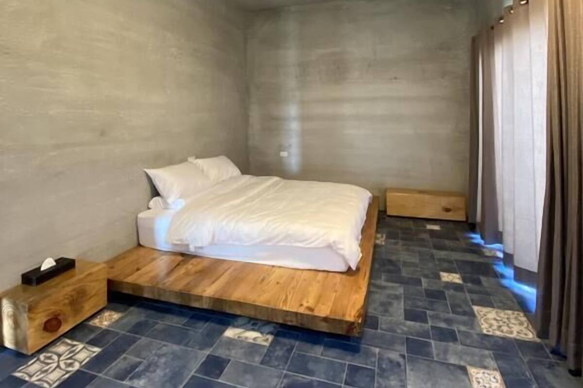 A bedroom with a wooden platform bed, a blue-tiled floor, and a ceiling light.