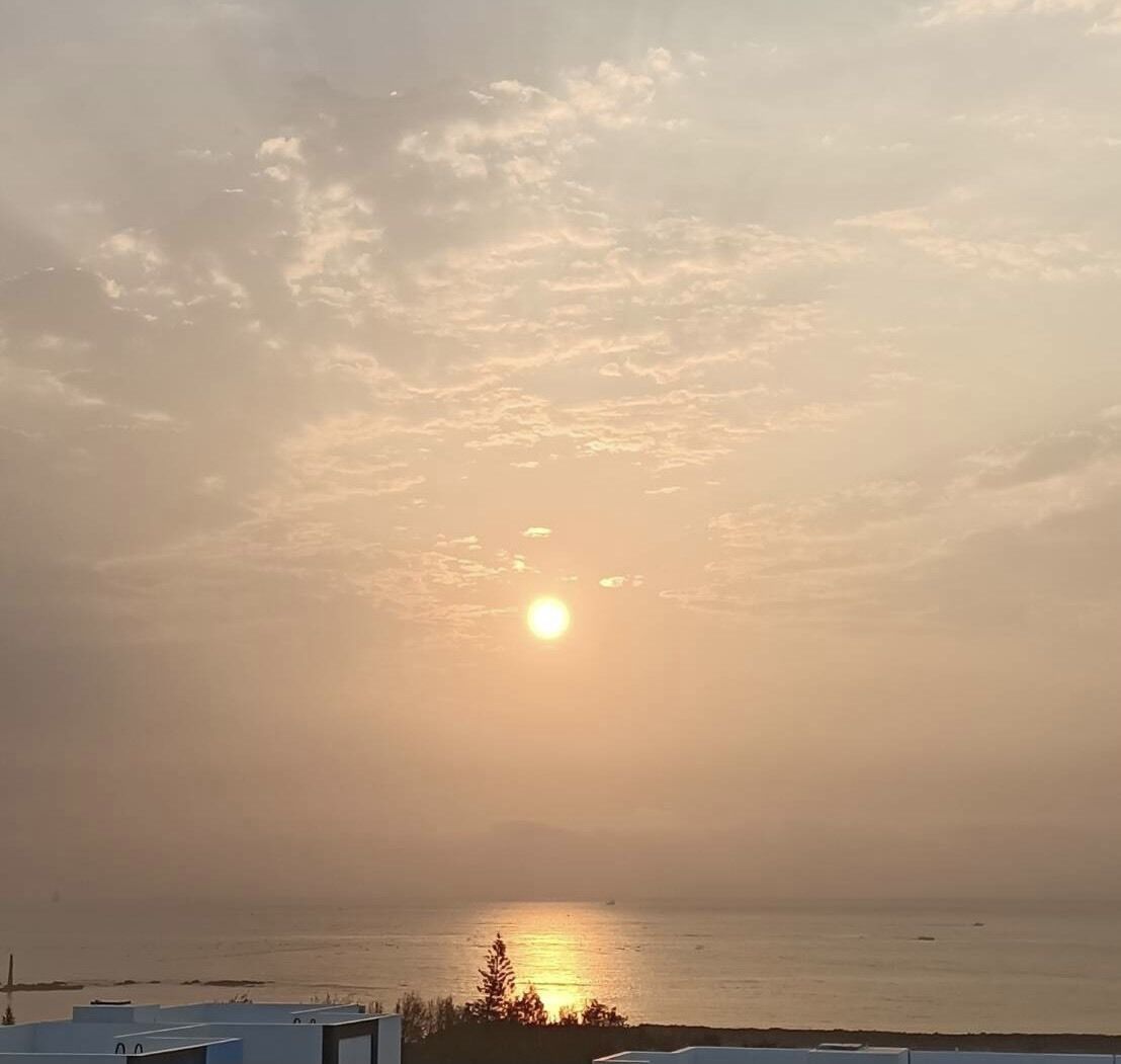 A sunset over a body of water with a clear horizon and a distant shoreline.