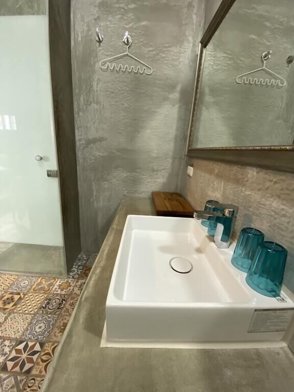Un baño con un lavabo blanco, vasos de vidrio azules y suelo de baldosas estampadas.