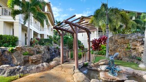 Un patio de hotel con una cascada de roca, una pérgola metálica y jardines tropicales.