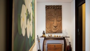 A hallway with a wooden floor, a painting of flowers, a wooden sculpture, and a table with decorative items. - Kata gardens 2 bedroom near Kata beach 3B (Karon)