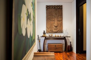 A hallway with a wooden floor, a painting of flowers, a wooden sculpture, and a table with decorative items. - Kata gardens 2 bedroom near Kata beach 3B (Karon)