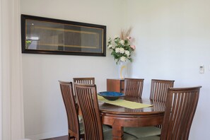A dining area with a round wooden table, six wooden chairs, a vase with flowers, and a framed picture on the wall. - Kata gardens 2 bedroom near Kata beach 3B (Karon)