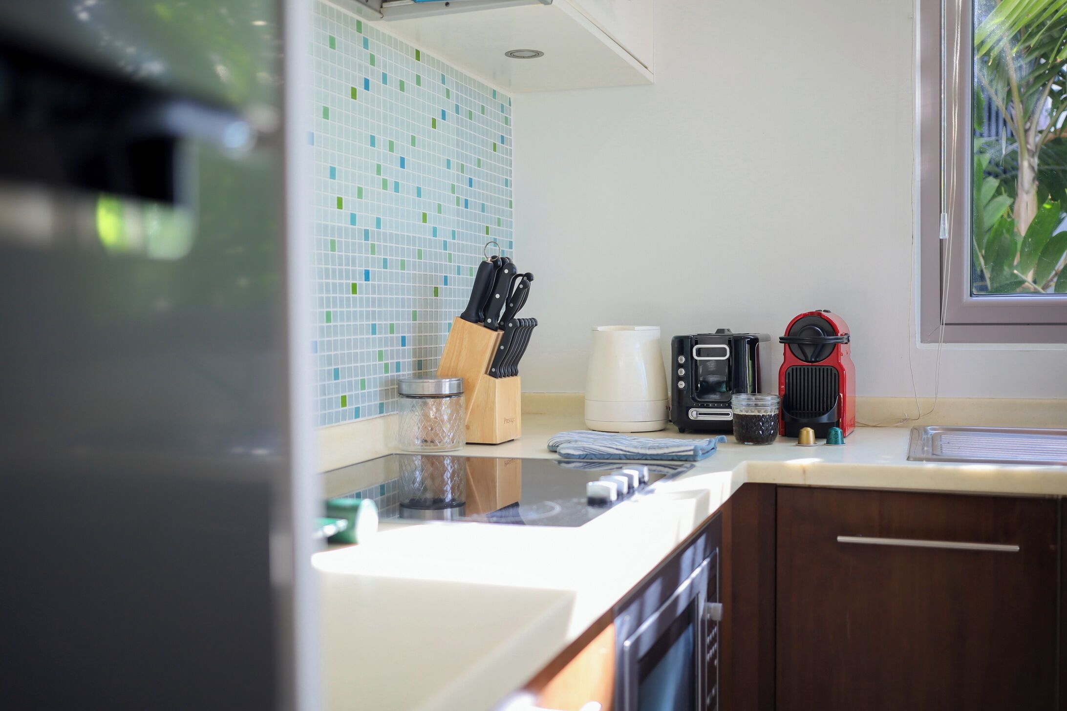Una cocina con salpicadero de azulejos, cafetera, hervidor y ventana con vistas a zonas verdes.