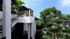 A modern building with a white exterior, a balcony with a wooden door, and lush greenery around. - Kata gardens 2 bedroom near Kata beach 3B (Karon)