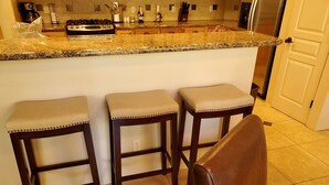 A kitchen with three bar stools, a stainless steel refrigerator, and a gas stove.