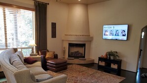 A living room with a sofa, armchair, ottoman, fireplace, TV, and a decorative rug.