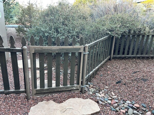 A wooden fence with a gate, a stone pathway, and a gravel area with small rocks.
