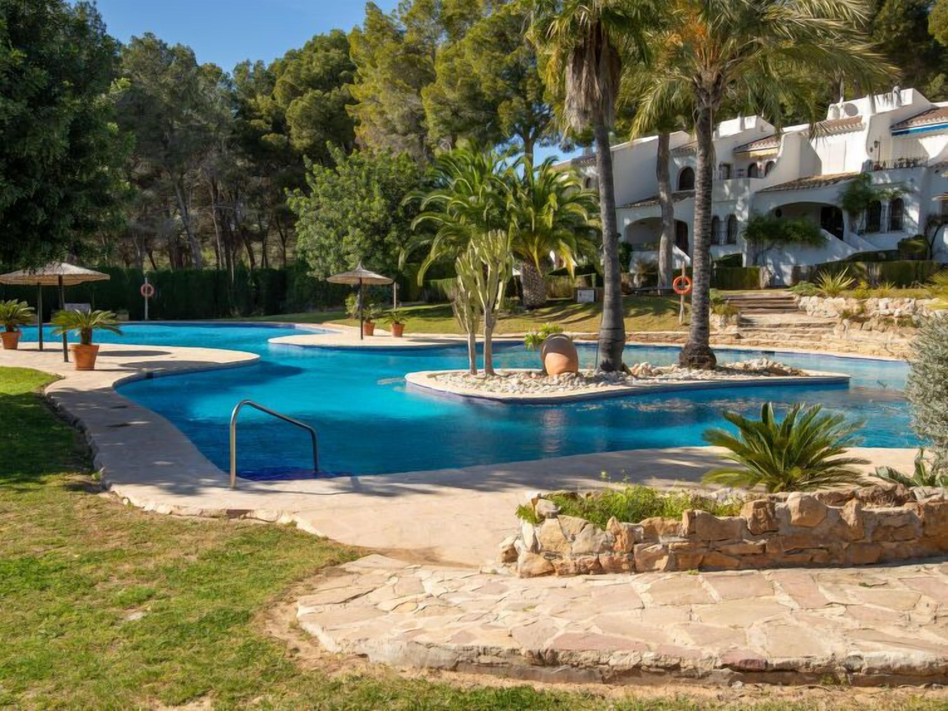 A resort with a large, winding pool surrounded by palm trees and a stone wall.