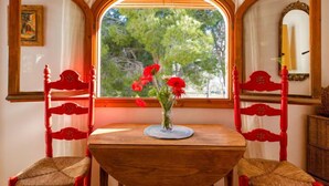 A room with a wooden table and two red chairs, a window with a view of trees, and a mirror on the wall. - Los Lagos by Interhome (Dénia)
