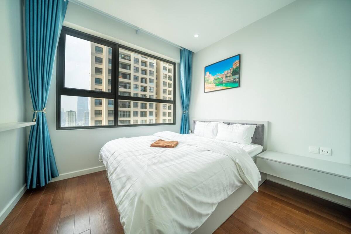 A bedroom with a large window, a bed, a bench, and a painting on the wall.