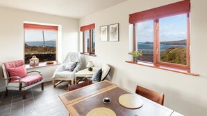 A dining area with a view of the sea, a table with placemats, two chairs, and a lamp.