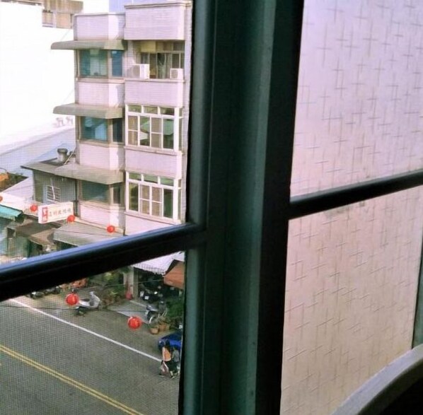 Vista desde una ventana de un edificio de varios pisos, que muestra un estacionamiento con vehículos y una pequeña construcción con techo rojo.