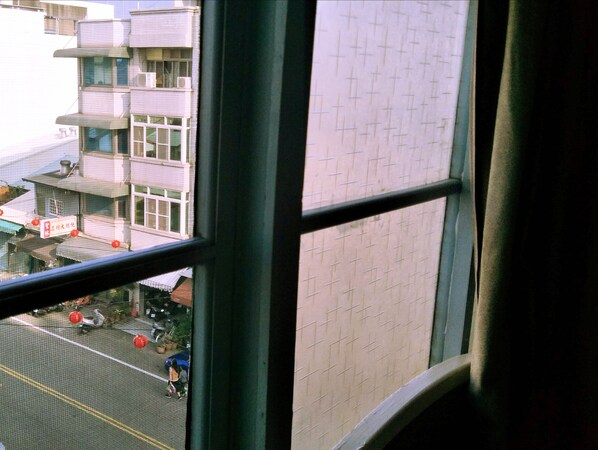 A view through a window with a grid pattern on the wall, a building with multiple floors, and a street scene with parked vehicles and people. - Pon Kan Inn (Beigang)