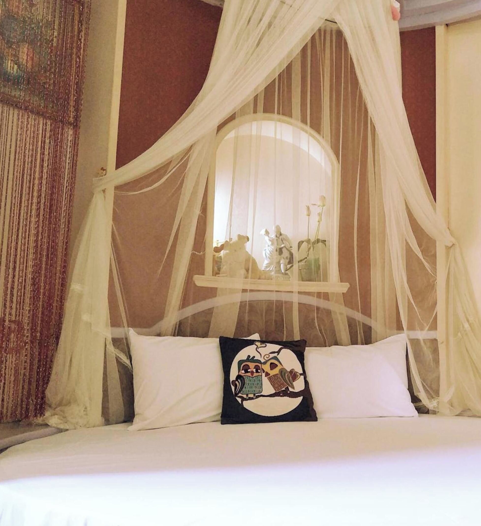 A bed with a canopy, a pillow with a cartoon character, and a window with a view of a statue.