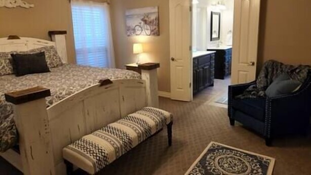 Une chambre à coucher comprenant un lit, un banc, une chaise et une porte donnant sur une salle de bain.
