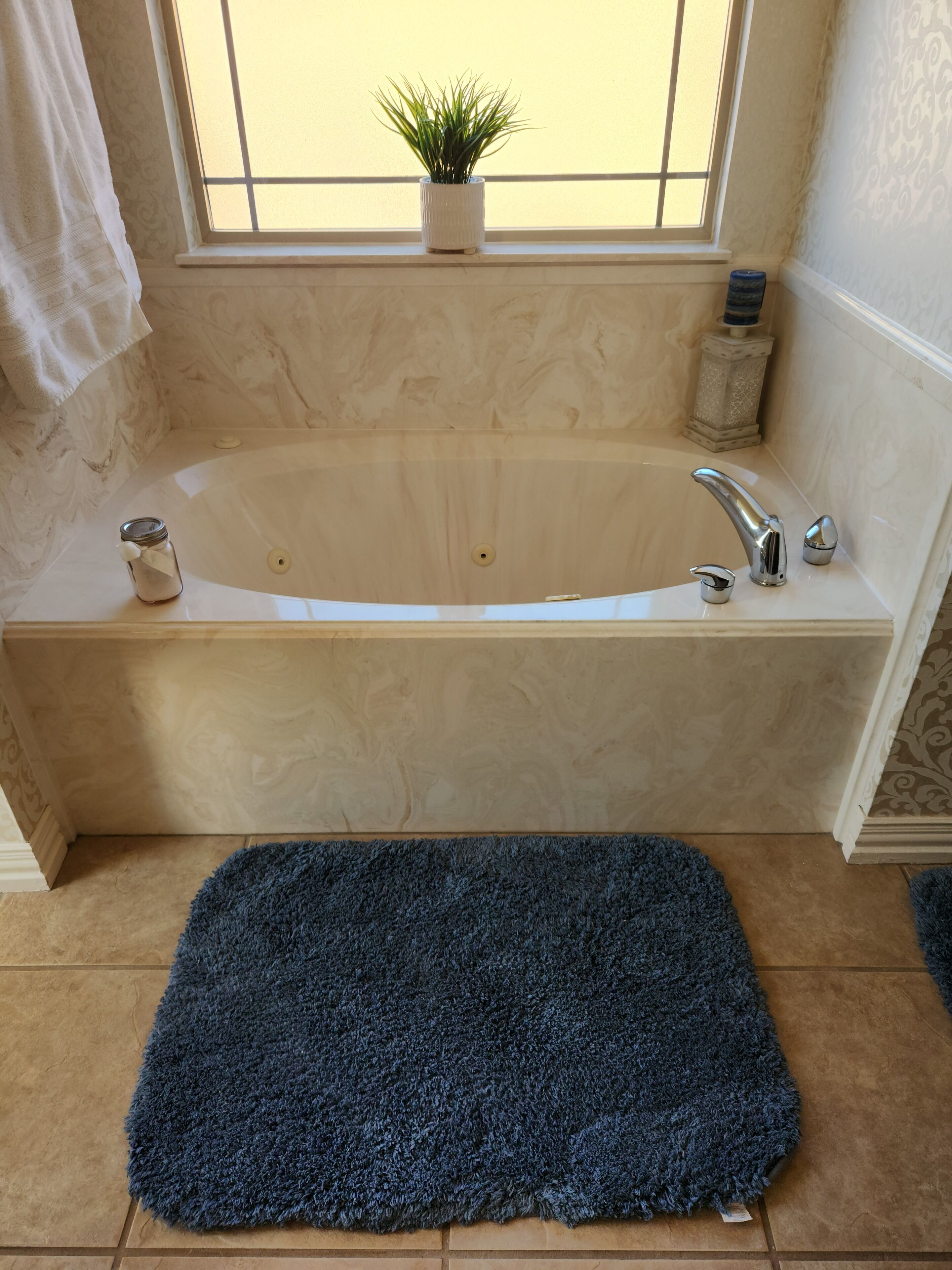 A bathroom with a bathtub, a window, a potted plant, a towel, and a blue rug.