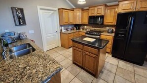 Une cuisine dotée de plans de travail en granit, d’armoires en bois, d’un réfrigérateur noir et d’un four à micro-ondes.