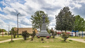 Et monument i en græsplæne med træer og en bygning i baggrunden.