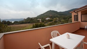 A balcony with a table and chairs, overlooking a hilly landscape with houses. - APP.TI NORSI - NORSI - MONO (Capoliveri)