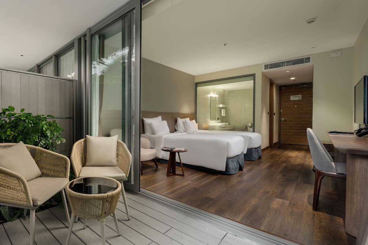 Une chambre d’hôtel moderne dotée d’un grand lit, d’un coin salon avec des fauteuils en osier, d’une petite table ronde et d’un bureau en bois.