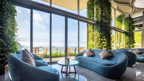 Zona d'estar moderna amb sofàs blaus i una taula de centre de vidre, grans finestres amb vista al mar i jardins verticals verds.