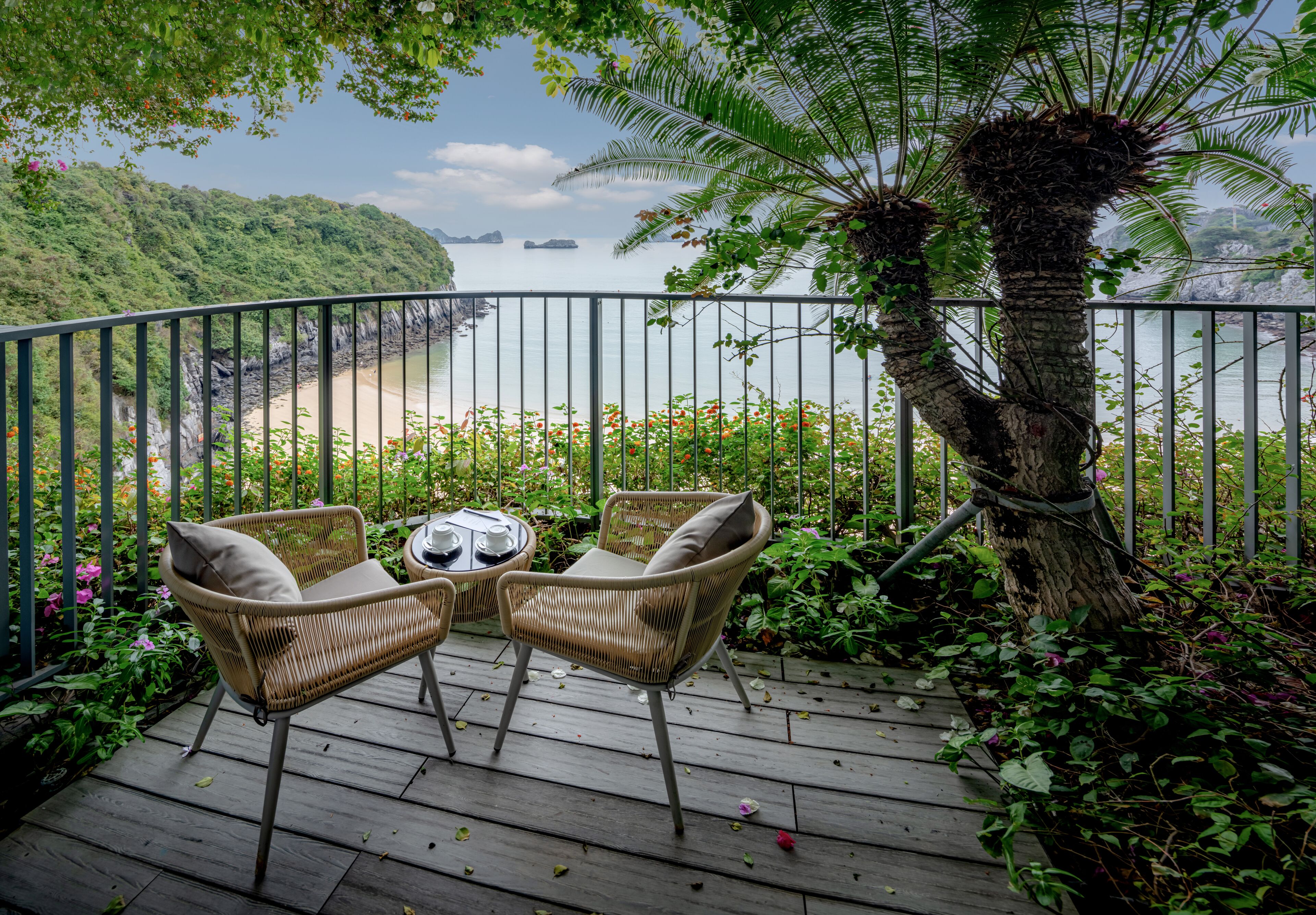 Terraza de madera con sillas de mimbre y una mesa, con vistas a la playa y al océano.