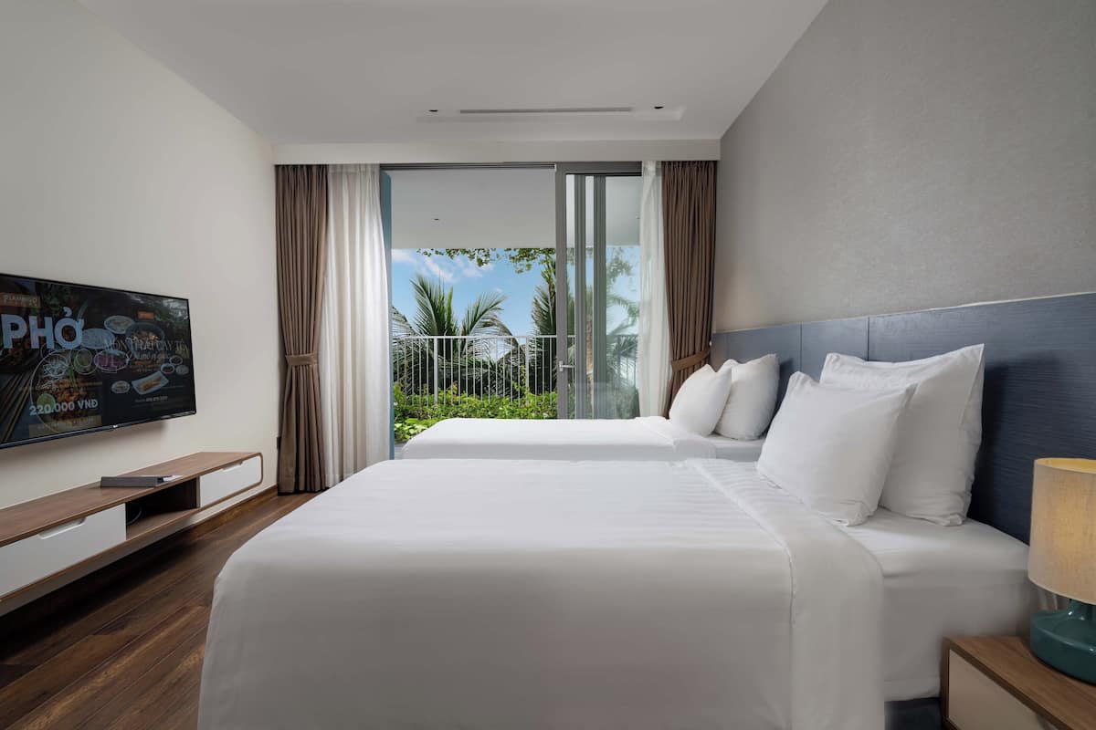 Une chambre d’hôtel avec deux lits, une télévision et un balcon avec des rideaux.
