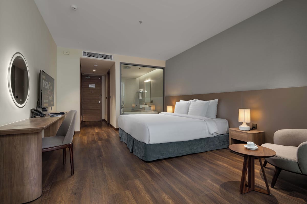 Une chambre d’hôtel comprenant un lit, une table de chevet, une lampe, une chaise, un bureau et un miroir.