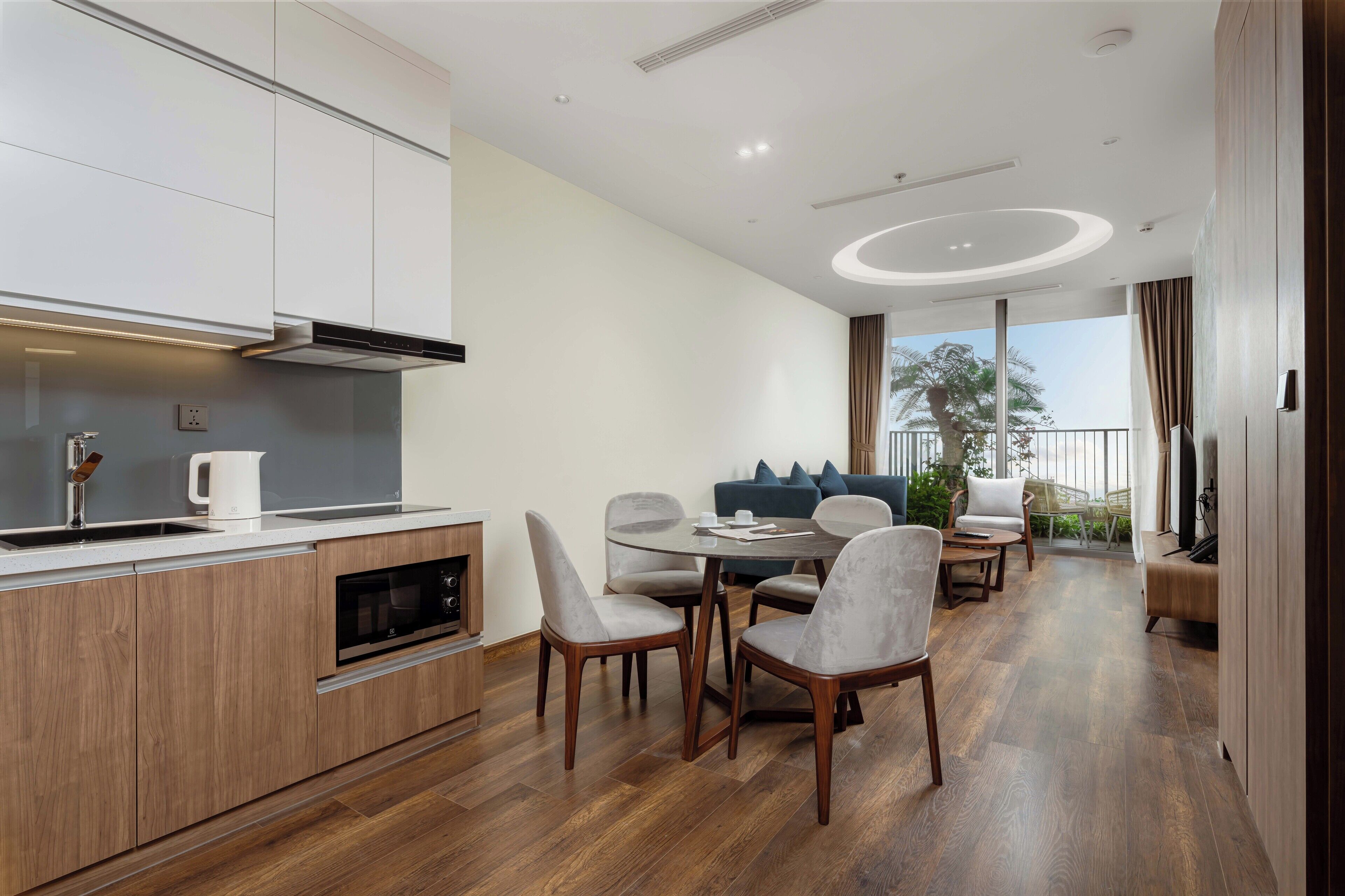 A modern kitchen with built-in appliances, a dining area with a round table and chairs, and a balcony with a view of the outdoors.