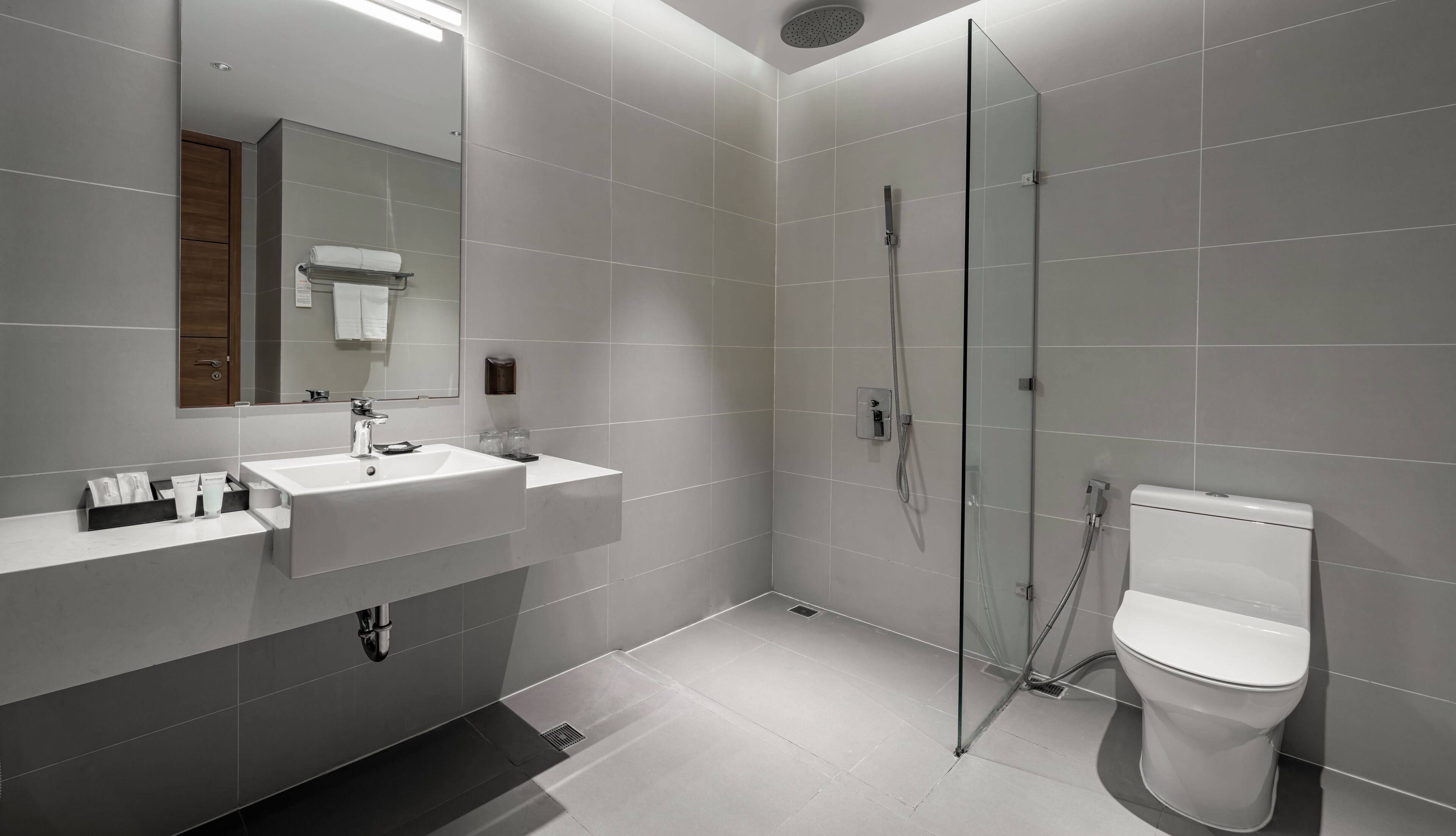 Een moderne badkamer met een grote spiegel, twee wastafels, een toilet en een douche met glazen wanden.