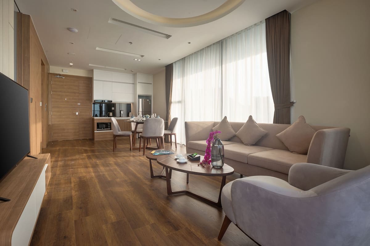 Un salon moderne avec un canapé, des fauteuils et une table basse. On y trouve également un coin repas avec des chaises et une table, ainsi qu’une cuisine à l’arrière-plan.