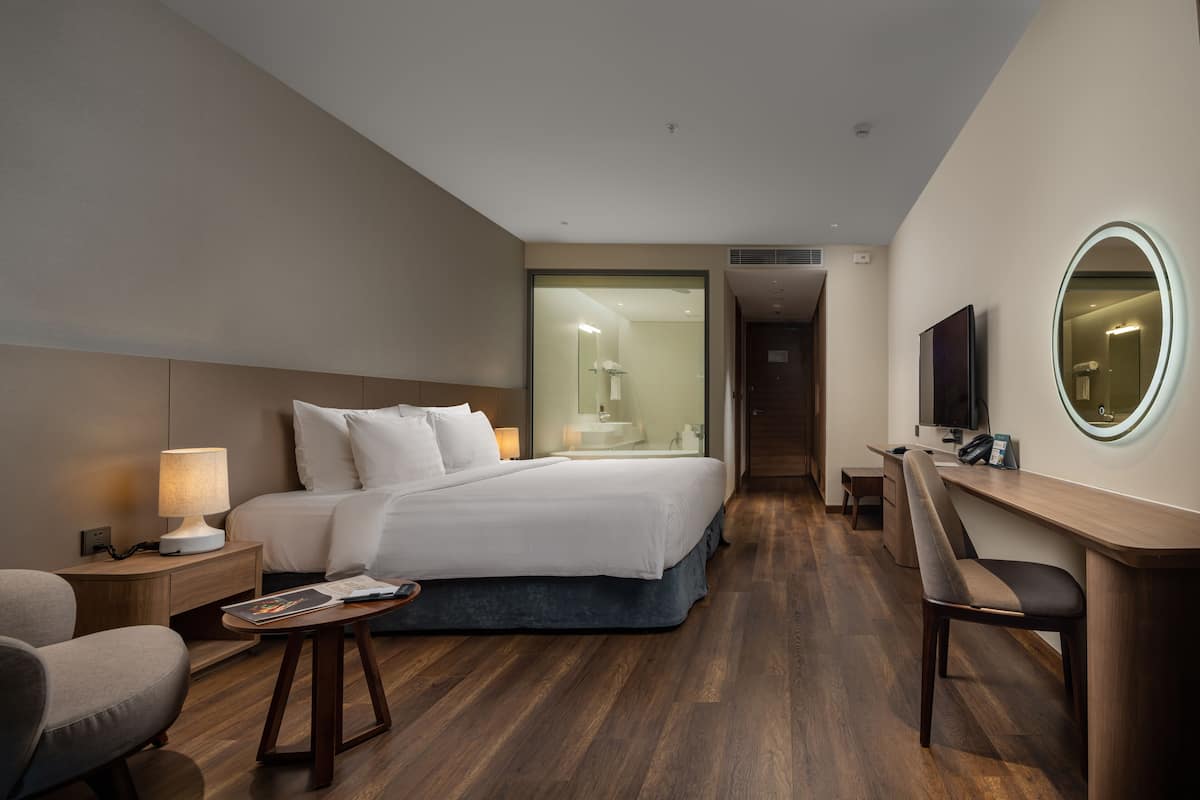 Une chambre d’hôtel moderne dotée d’un grand lit, de tables de chevet, d’un bureau avec une chaise, d’une télévision et d’un miroir.