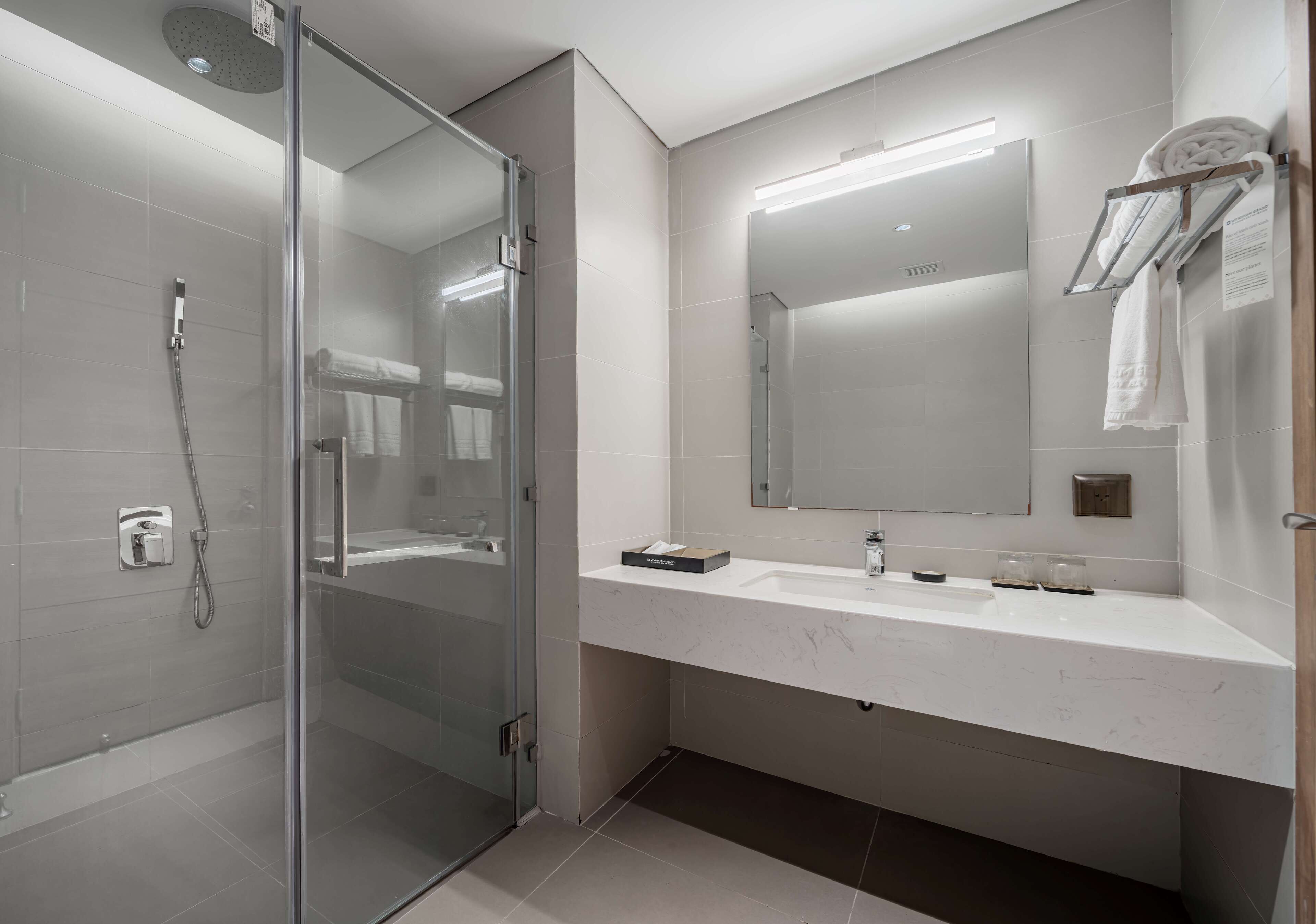 Uma casa de banho moderna com chuveiro envidraçado, um espelho grande e um lavatório branco com suporte para toalhas.