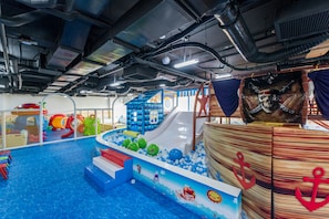 An indoor play area with a pool, slides, and themed play structures.