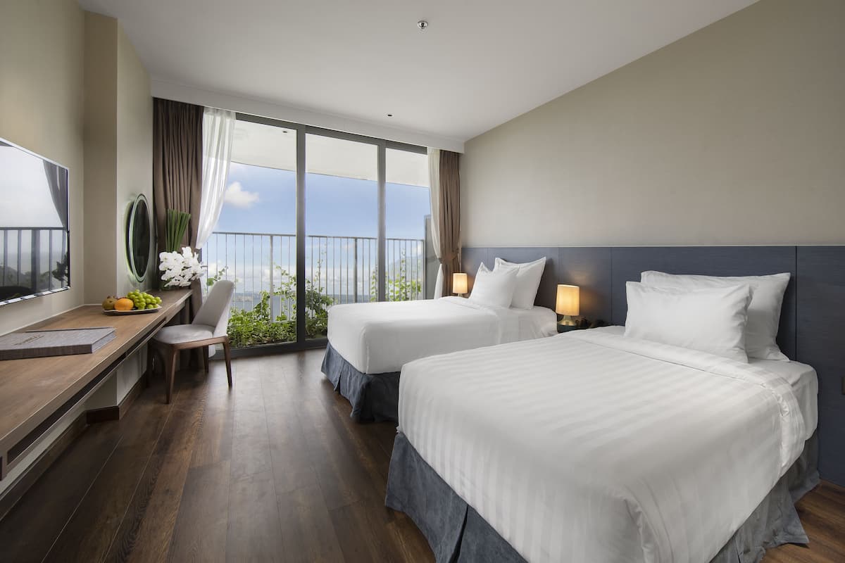 Une chambre d’hôtel avec deux lits, un bureau avec une chaise, une télévision et un balcon avec vue.