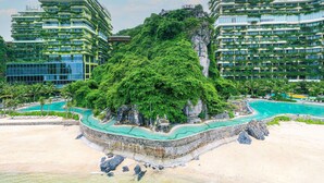 Un complex turístic amb diversos edificis alts, una formació rocosa central i una zona de piscina.