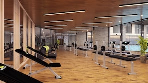 A modern gym with wooden floors, exercise equipment, and large windows.