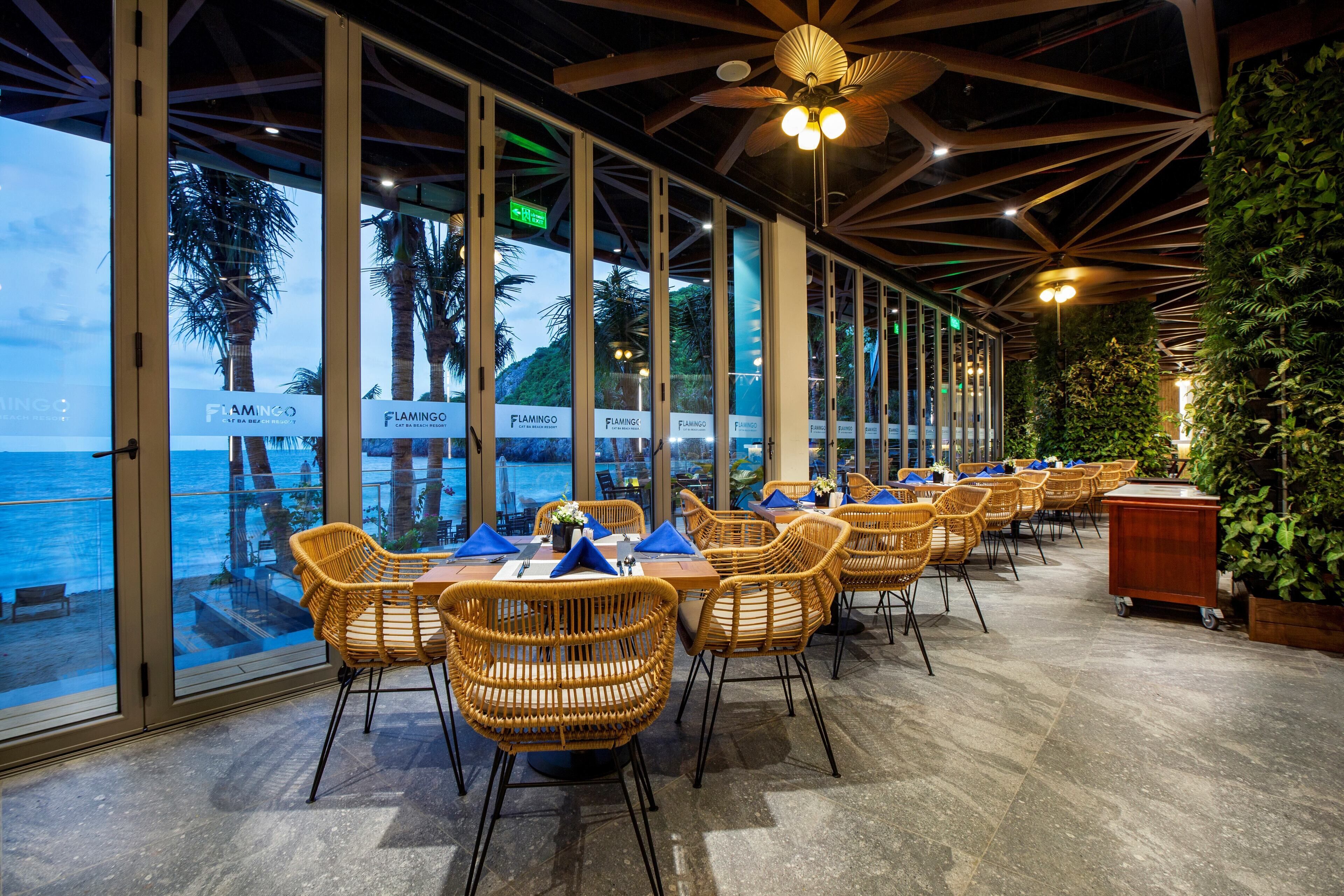 Een restaurant met grote ramen, rieten stoelen en uitzicht op zee.