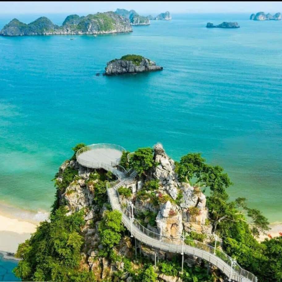 A coastal landscape with a winding pathway leading to a viewpoint over turquoise waters and distant islands.