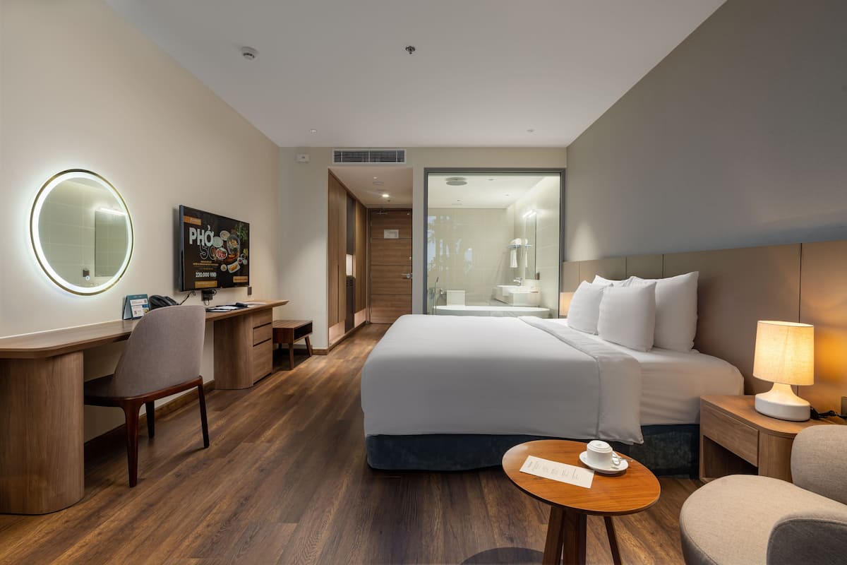 Une chambre d’hôtel avec un lit, un bureau, une chaise et un miroir rond.