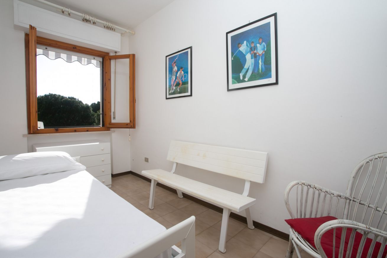 A bedroom with a bed, a white bench, a chair, and two framed pictures on the wall.