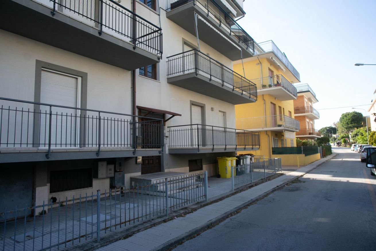 Un edificio residenziale a più piani con balconi, un cancello e vista sulla strada.