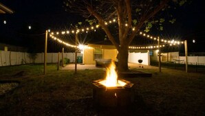 Un jardin avec un foyer, des guirlandes lumineuses et un arbre.