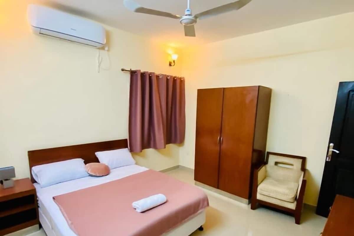 A hotel room with a bed, a wardrobe, a chair, a desk, and a ceiling fan.