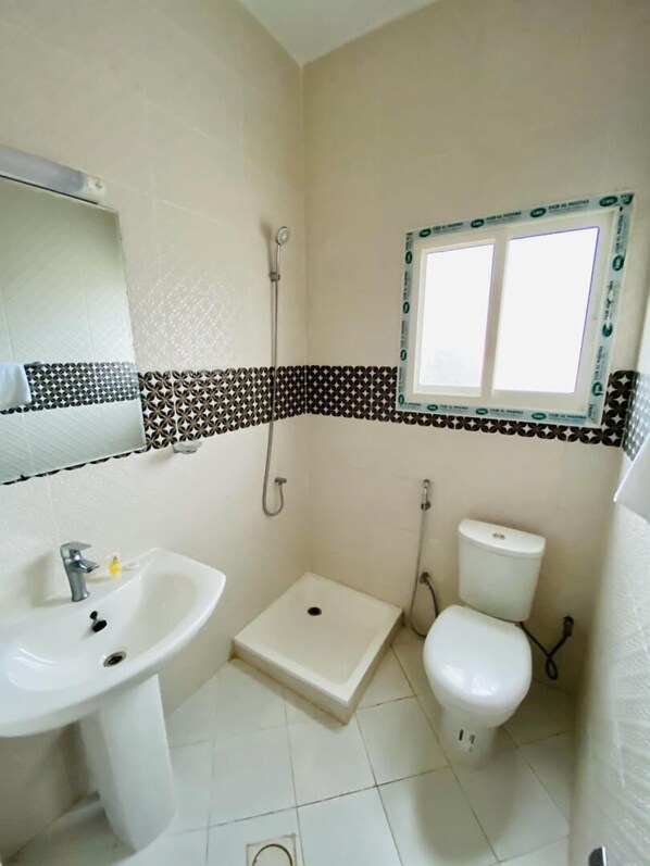 A bathroom with a sink, toilet, shower, and a window.