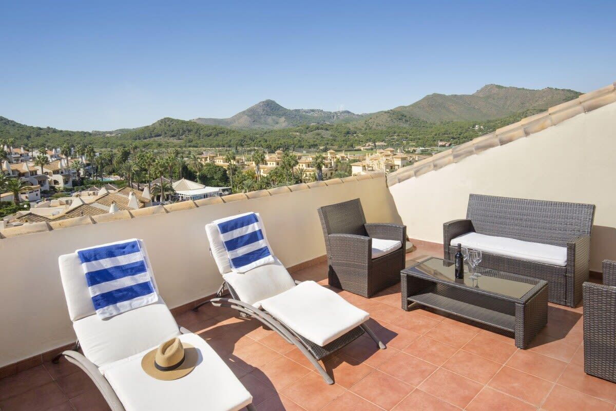 Une terrasse équipée de deux chaises longues, d ’un canapé en osier et d’une table basse en verre.